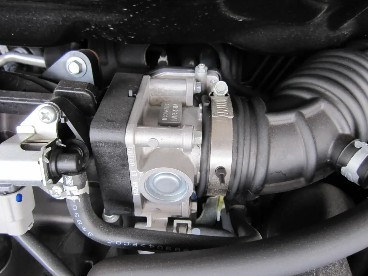 日産HR15DEエンジンの電子制御スロットルの例です。中央の銀色ユニットが吸気管の途中にあり、内部のモーターがECUの指示で弁を動かします。モーターや弁そのものは、この外観写真では見えません。